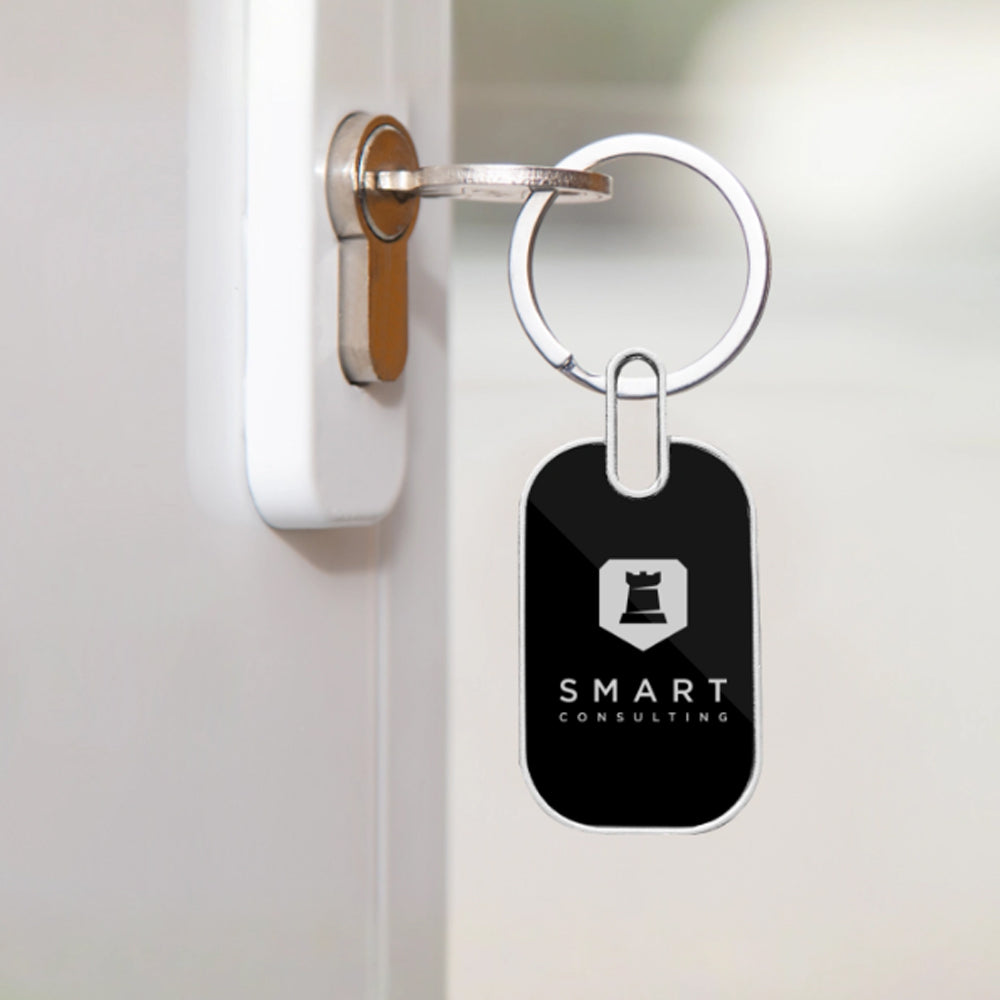 A silver key is in a white door lock, attached to an Oval Metal Keychain featuring custom branding—a black chess rook icon and "SMART CONSULTING"—making this Oval Metal Keychains product ideal promotional merchandise.