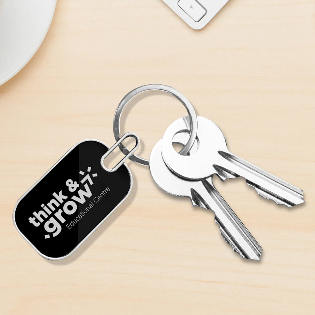 Two silver keys on a metal keyring with an Oval Metal Keychain featuring custom branding for think & grow7 Educational Centre, displayed on a light wood surface—ideal as promotional merchandise.