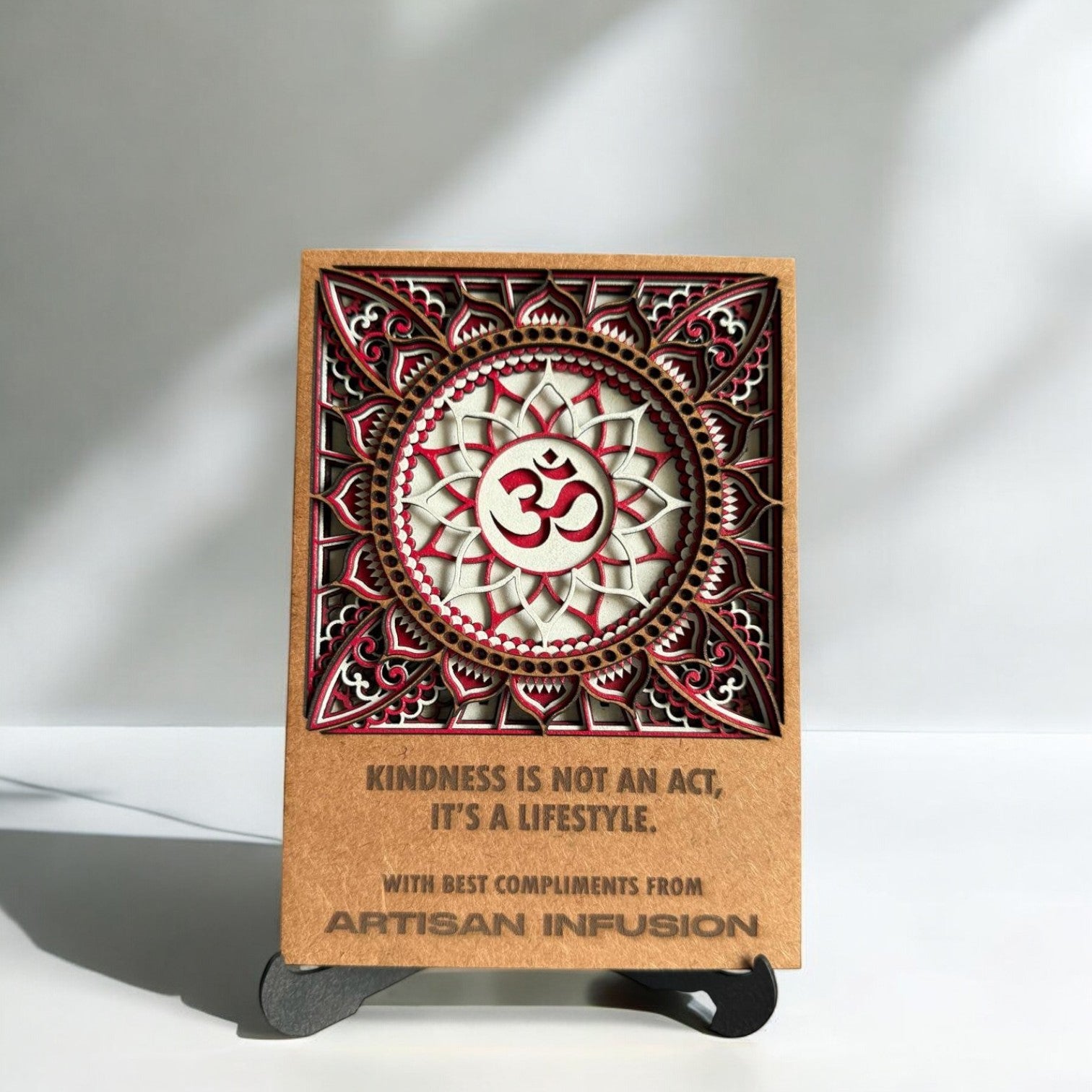 The Omm Mandala Art - Table Top is a decorative card with the Om symbol centered, ideal for meditation décor. It features the quote: “KINDNESS IS NOT AN ACT, IT’S A LIFESTYLE. WITH BEST COMPLIMENTS FROM ARTISAN INFUSION.”.