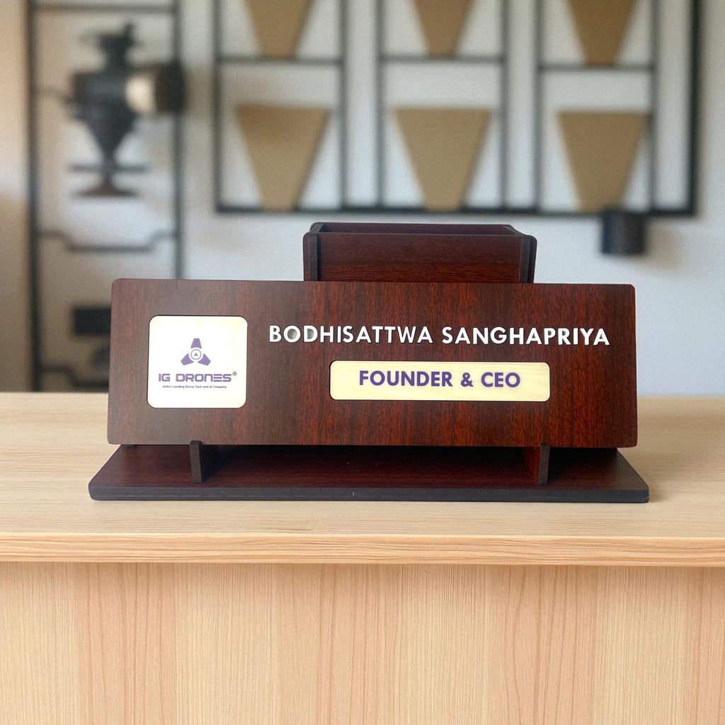 A Premium Wooden Desk Name Plate with Pen Holder, custom-engraved with Bodhisattwa Sanghapriya and FOUNDER & CEO alongside the IG Drones logo, sits on a light wood desk—an ideal Corporate Gift for any executive office.